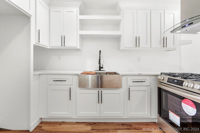 kitchen with exhaust hood, white cabinetry, stainless steel range with gas cooktop, and light hardwood / wood-style floors