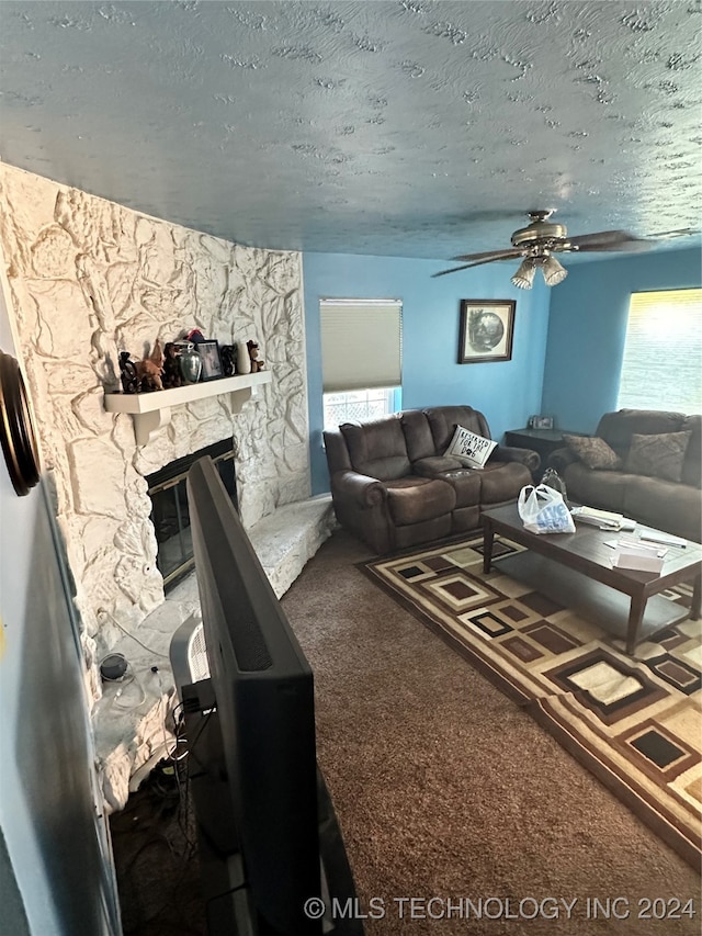 carpeted living room with a stone fireplace, a textured ceiling, and ceiling fan