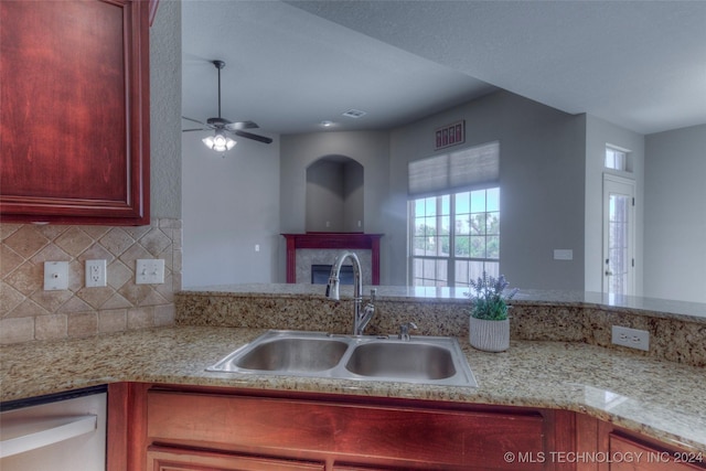 kitchen featuring sink, stainless steel dishwasher, ceiling fan, a tiled fireplace, and backsplash