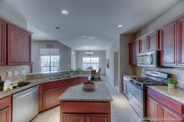 kitchen featuring sink, appliances with stainless steel finishes, hanging light fixtures, a notable chandelier, and a kitchen island