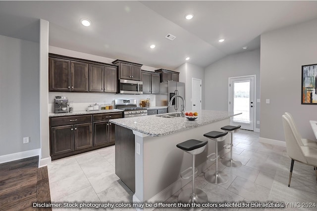 kitchen with lofted ceiling, an island with sink, appliances with stainless steel finishes, a kitchen bar, and sink