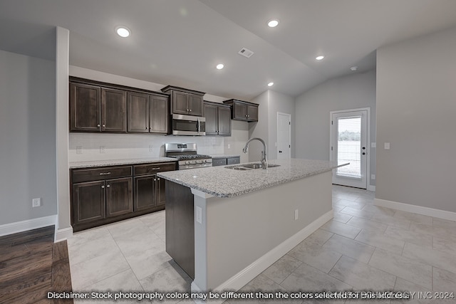 kitchen with a kitchen island with sink, stainless steel appliances, sink, vaulted ceiling, and light stone countertops