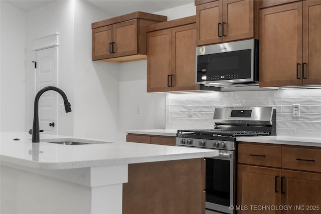 10804 S 274th Ave E, Coweta, OK 74429 - kitchen featuring appliances with stainless steel finishes, a sink, decorative backsplash, brown cabinetry, and light stone counters