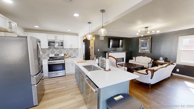 kitchen featuring stainless steel appliances, a center island with sink, decorative light fixtures, white cabinets, and light hardwood / wood-style floors