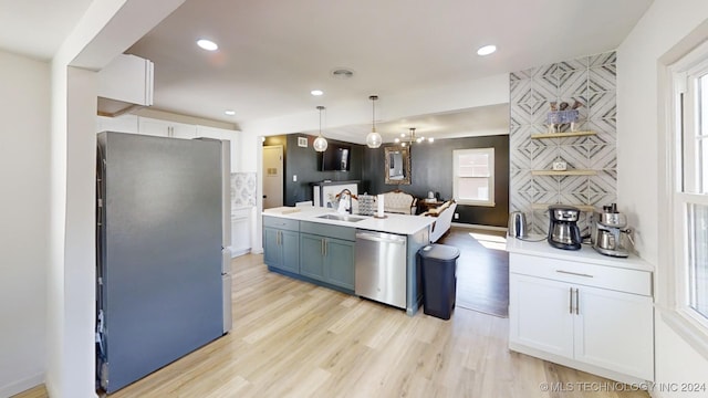 kitchen with appliances with stainless steel finishes, sink, hanging light fixtures, white cabinets, and light hardwood / wood-style flooring