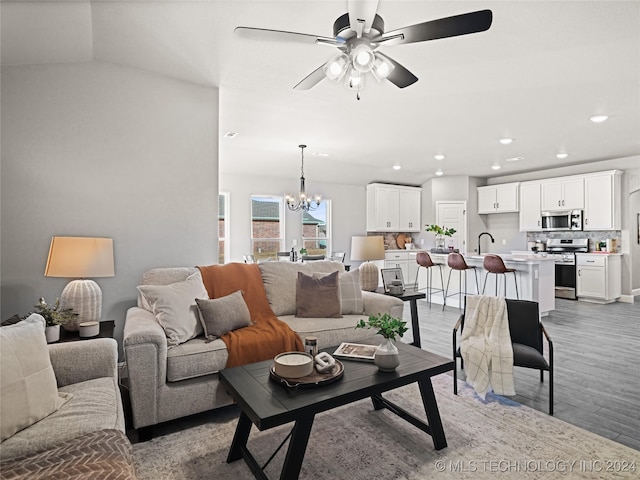 living room featuring hardwood / wood-style flooring, sink, ceiling fan with notable chandelier, and vaulted ceiling