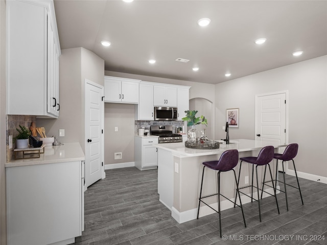 kitchen featuring decorative backsplash, an island with sink, appliances with stainless steel finishes, white cabinetry, and dark hardwood / wood-style floors