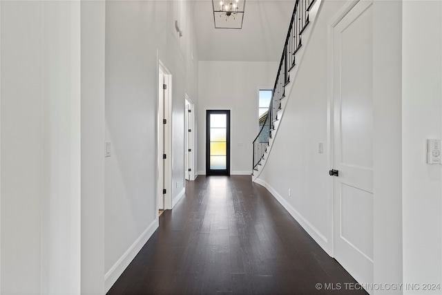 hallway with dark hardwood / wood-style floors, a towering ceiling, and a chandelier