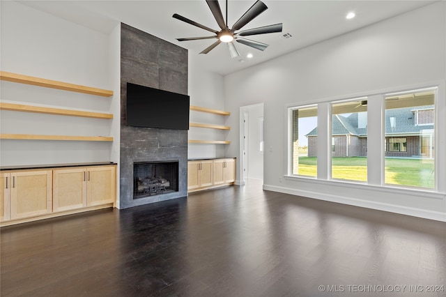 unfurnished living room featuring a towering ceiling, dark hardwood / wood-style floors, ceiling fan, and a tiled fireplace