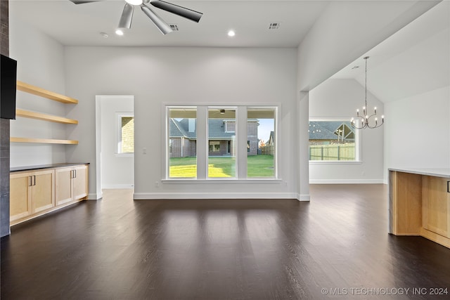 unfurnished living room with ceiling fan with notable chandelier, a wealth of natural light, and dark wood-type flooring