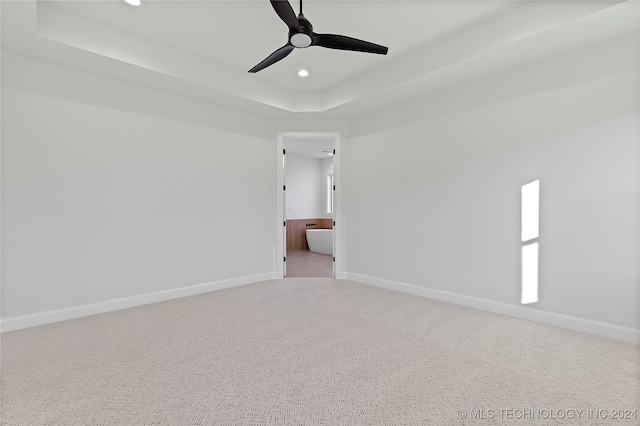 spare room with a tray ceiling, light carpet, and ceiling fan