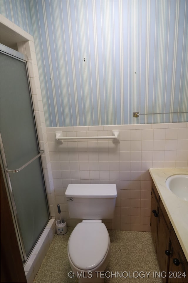 bathroom featuring vanity, toilet, tile walls, and a shower with door