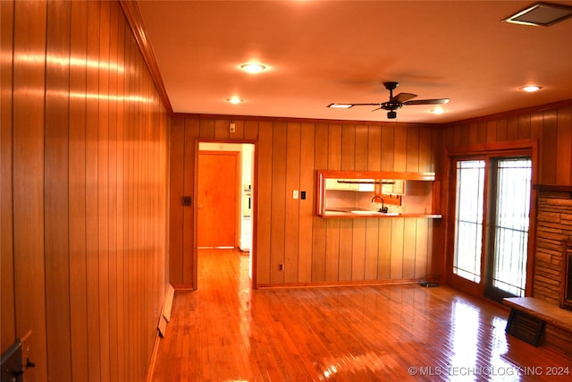 unfurnished living room featuring hardwood / wood-style floors, a fireplace, wooden walls, and ceiling fan