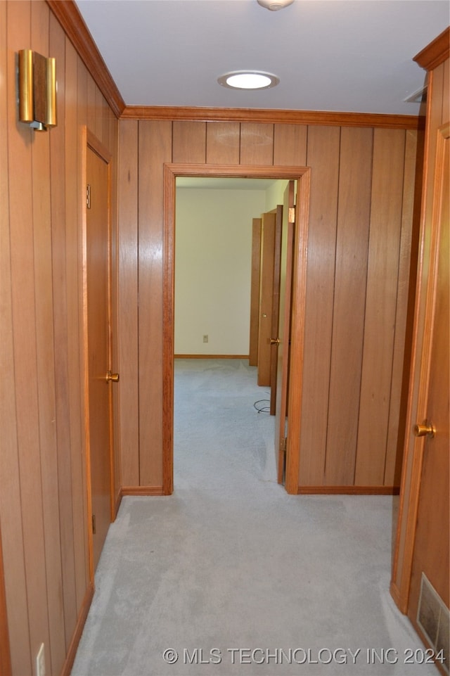 hall featuring ornamental molding, wooden walls, and light carpet