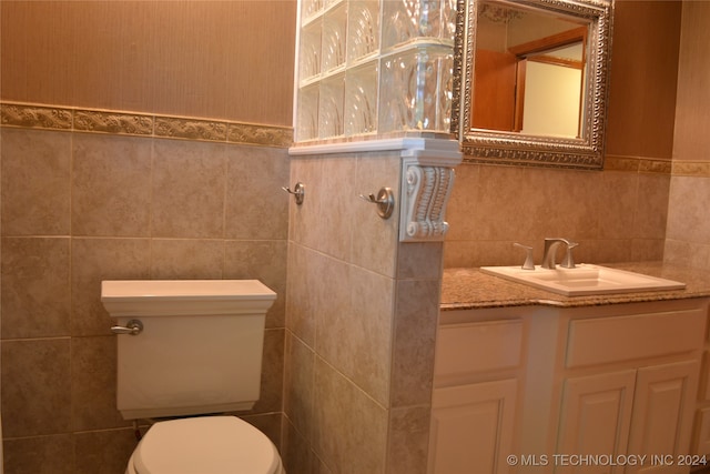 bathroom featuring toilet, vanity, and tile walls