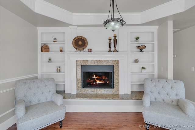 living area featuring crown molding, built in features, a fireplace, and hardwood / wood-style floors