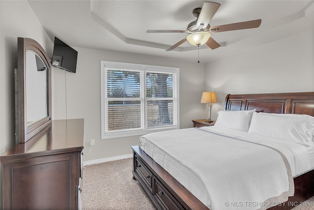 bedroom featuring light colored carpet, a tray ceiling, and ceiling fan