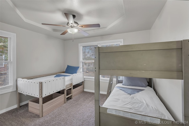 carpeted bedroom featuring a tray ceiling and ceiling fan