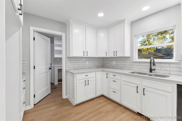 kitchen with white cabinets, backsplash, light stone countertops, light wood-type flooring, and sink