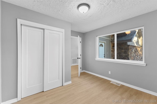 unfurnished bedroom with a closet, a textured ceiling, and light wood-type flooring