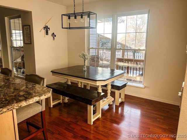 dining space featuring dark wood-type flooring, a healthy amount of sunlight, and a chandelier