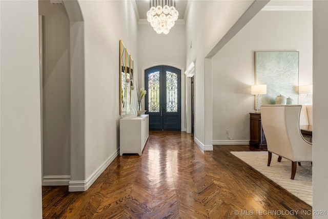 entryway featuring a towering ceiling, ornamental molding, dark parquet flooring, and an inviting chandelier