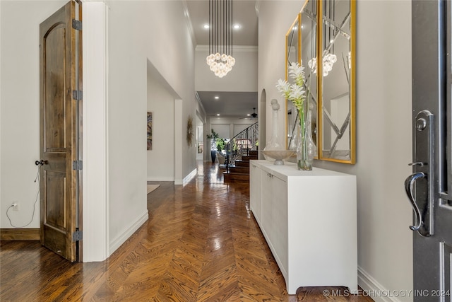 foyer with ornamental molding, a high ceiling, dark parquet floors, and ceiling fan with notable chandelier