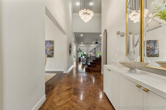 foyer featuring ornamental molding, a high ceiling, dark parquet flooring, and ceiling fan with notable chandelier