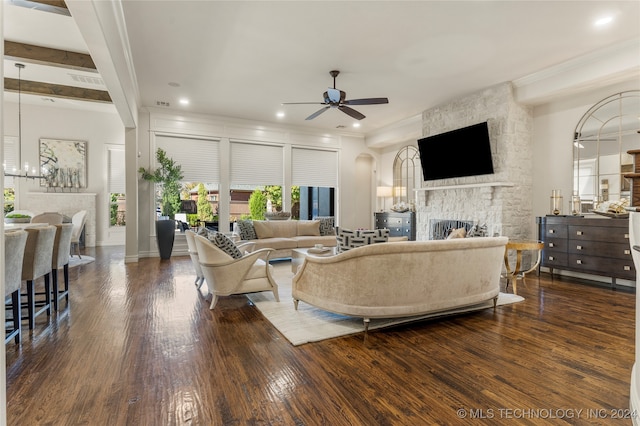 living room featuring crown molding, ceiling fan with notable chandelier, a stone fireplace, dark hardwood / wood-style flooring, and beam ceiling