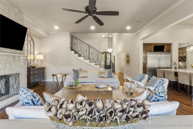 living room featuring a large fireplace, ornamental molding, sink, dark hardwood / wood-style flooring, and ceiling fan