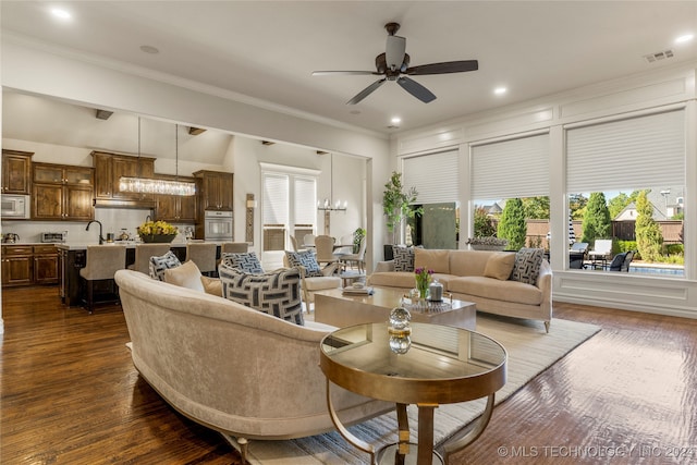 living room featuring dark wood-type flooring, crown molding, a wealth of natural light, and ceiling fan with notable chandelier