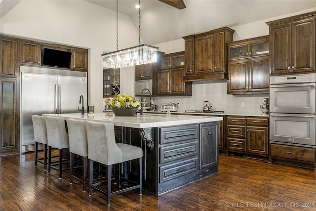 kitchen with a center island with sink, high vaulted ceiling, dark hardwood / wood-style floors, built in appliances, and dark brown cabinetry