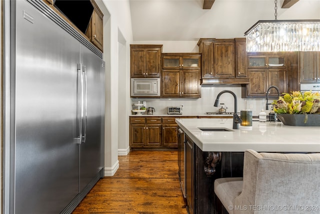 kitchen featuring built in appliances, dark wood-type flooring, a breakfast bar, and a chandelier