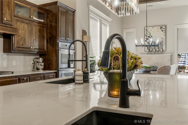 kitchen with stovetop, stainless steel double oven, dark brown cabinetry, and pendant lighting