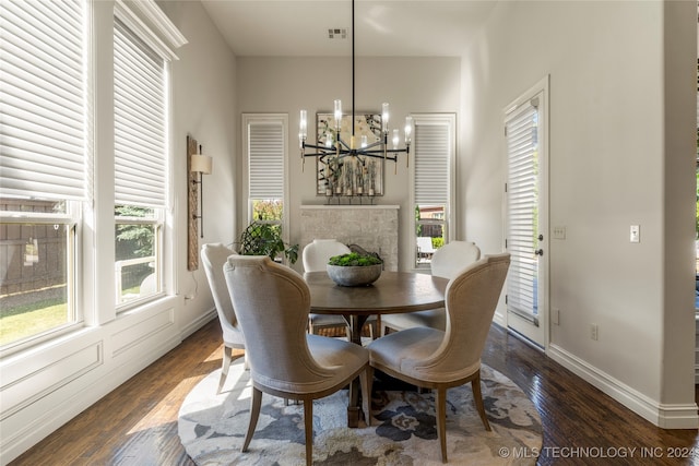 dining space with a stone fireplace, an inviting chandelier, and dark hardwood / wood-style floors