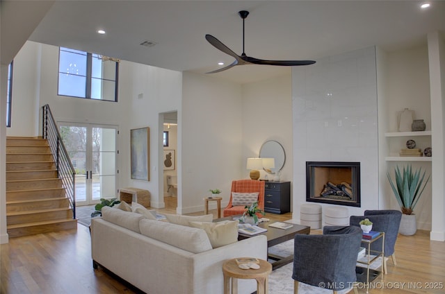 living room with built in shelves, ceiling fan, a tiled fireplace, and hardwood / wood-style flooring