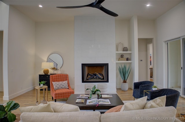 living room with ceiling fan, built in features, light wood-type flooring, and a fireplace