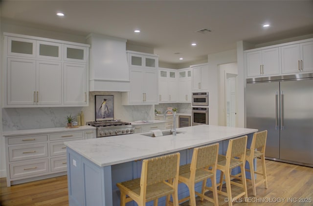 kitchen with white cabinets, sink, an island with sink, light stone counters, and stainless steel appliances