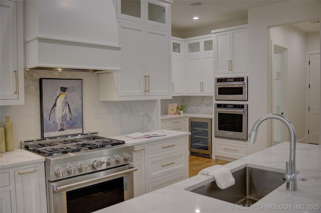 kitchen featuring premium range hood, light stone counters, stainless steel appliances, beverage cooler, and sink