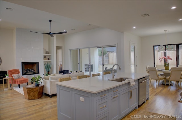 kitchen featuring light stone countertops, ceiling fan, sink, a center island with sink, and hanging light fixtures