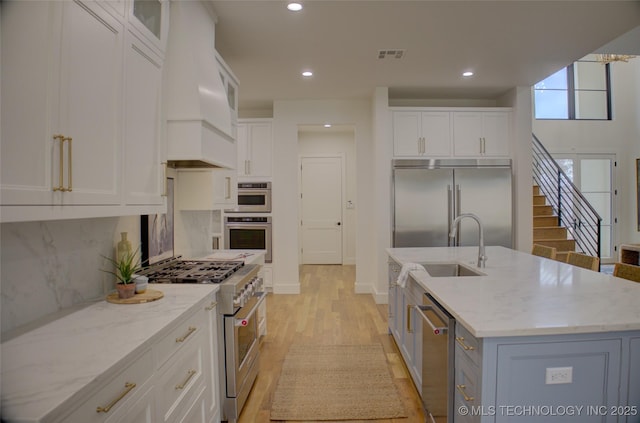 kitchen featuring white cabinetry, light stone countertops, light hardwood / wood-style flooring, an island with sink, and high end appliances