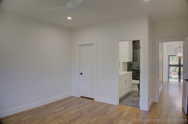 unfurnished bedroom featuring ceiling fan with notable chandelier, light wood-type flooring, and connected bathroom