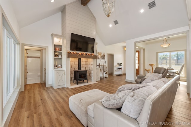 living room featuring a wood stove, high vaulted ceiling, light hardwood / wood-style floors, and beam ceiling