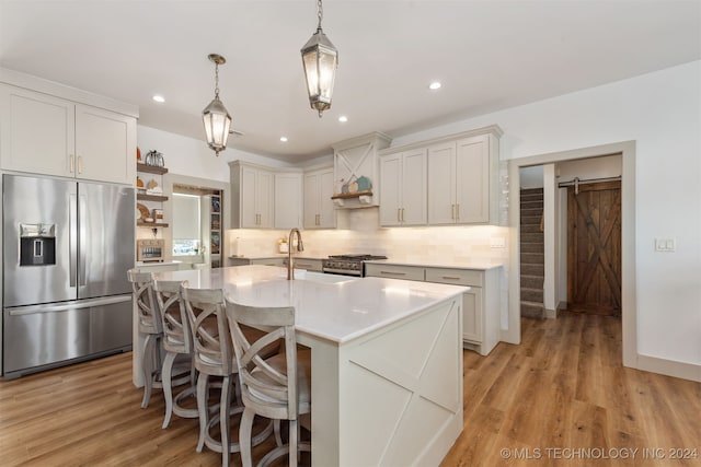 kitchen with stainless steel appliances, sink, decorative light fixtures, white cabinets, and a barn door