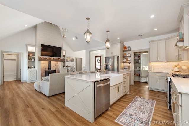 kitchen featuring stainless steel appliances, a center island with sink, hanging light fixtures, a wood stove, and light hardwood / wood-style flooring