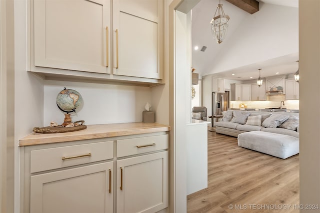 interior space with stainless steel fridge, decorative light fixtures, beam ceiling, light hardwood / wood-style floors, and custom exhaust hood