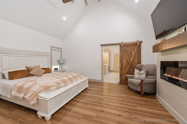 bedroom with light wood-type flooring, a barn door, ceiling fan, and high vaulted ceiling