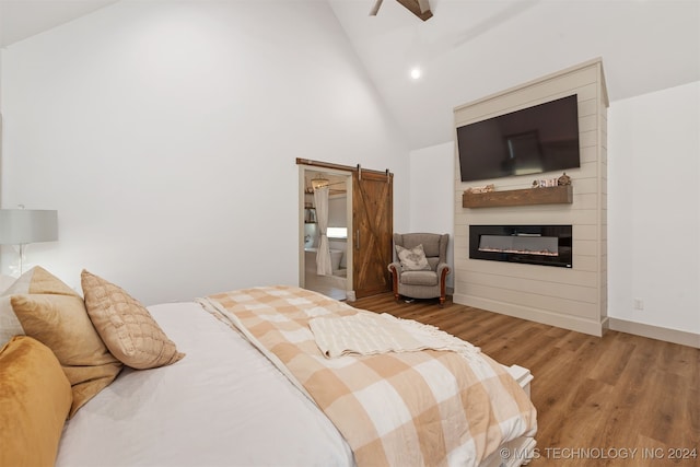 bedroom with a barn door, a large fireplace, high vaulted ceiling, and hardwood / wood-style floors