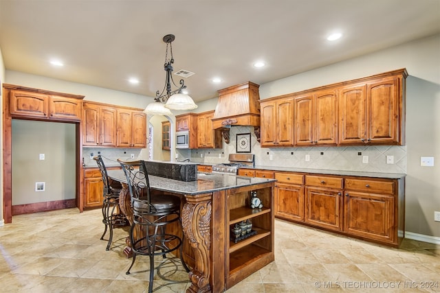 kitchen with a kitchen island, appliances with stainless steel finishes, a breakfast bar, dark stone counters, and decorative light fixtures