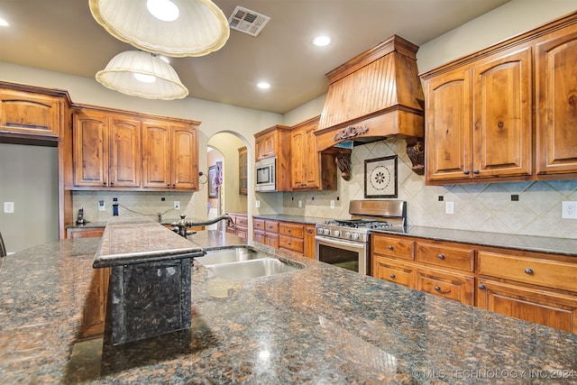 kitchen featuring backsplash, appliances with stainless steel finishes, dark stone counters, and premium range hood